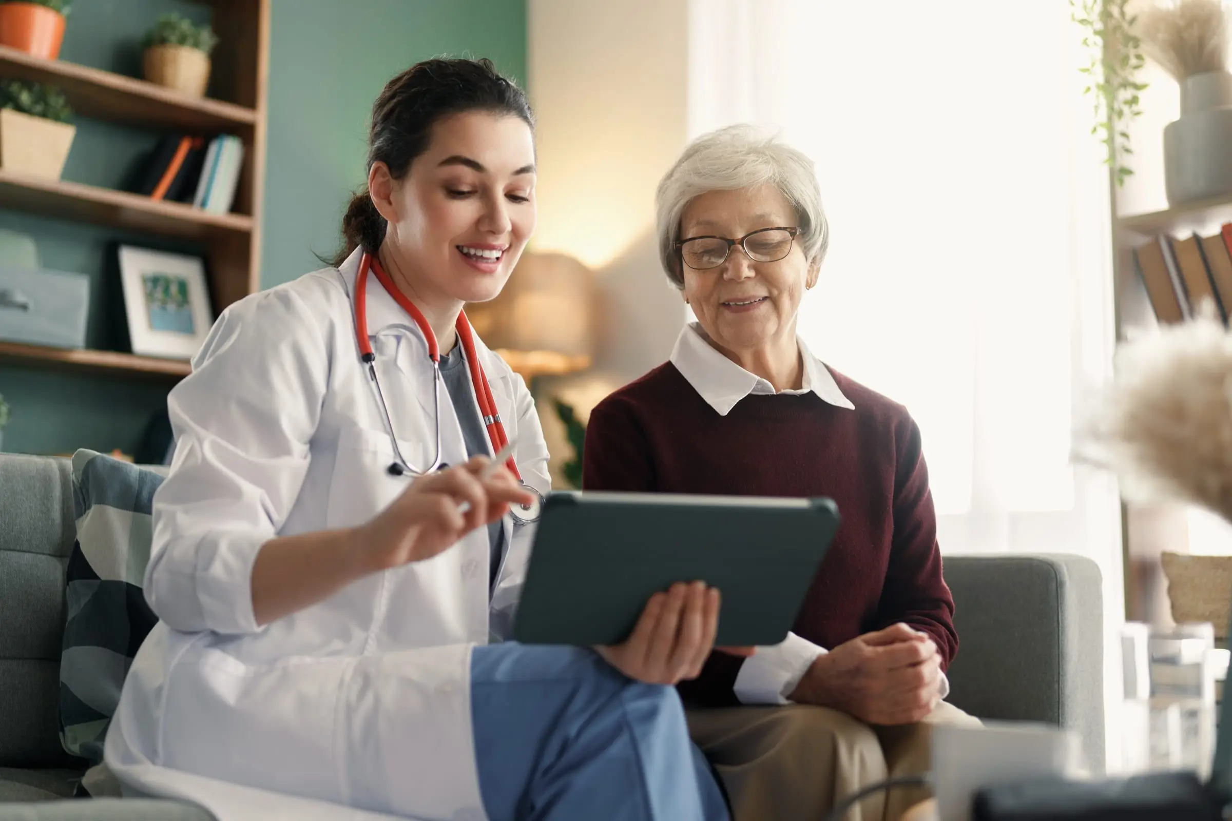 A clinician shows an older woman something on a tablet in her living room