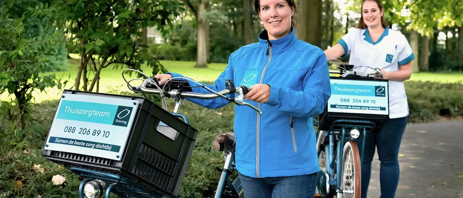 Two Omring home-care colleagues with their bikes, Thuiszorgteam signage on the carrier crates