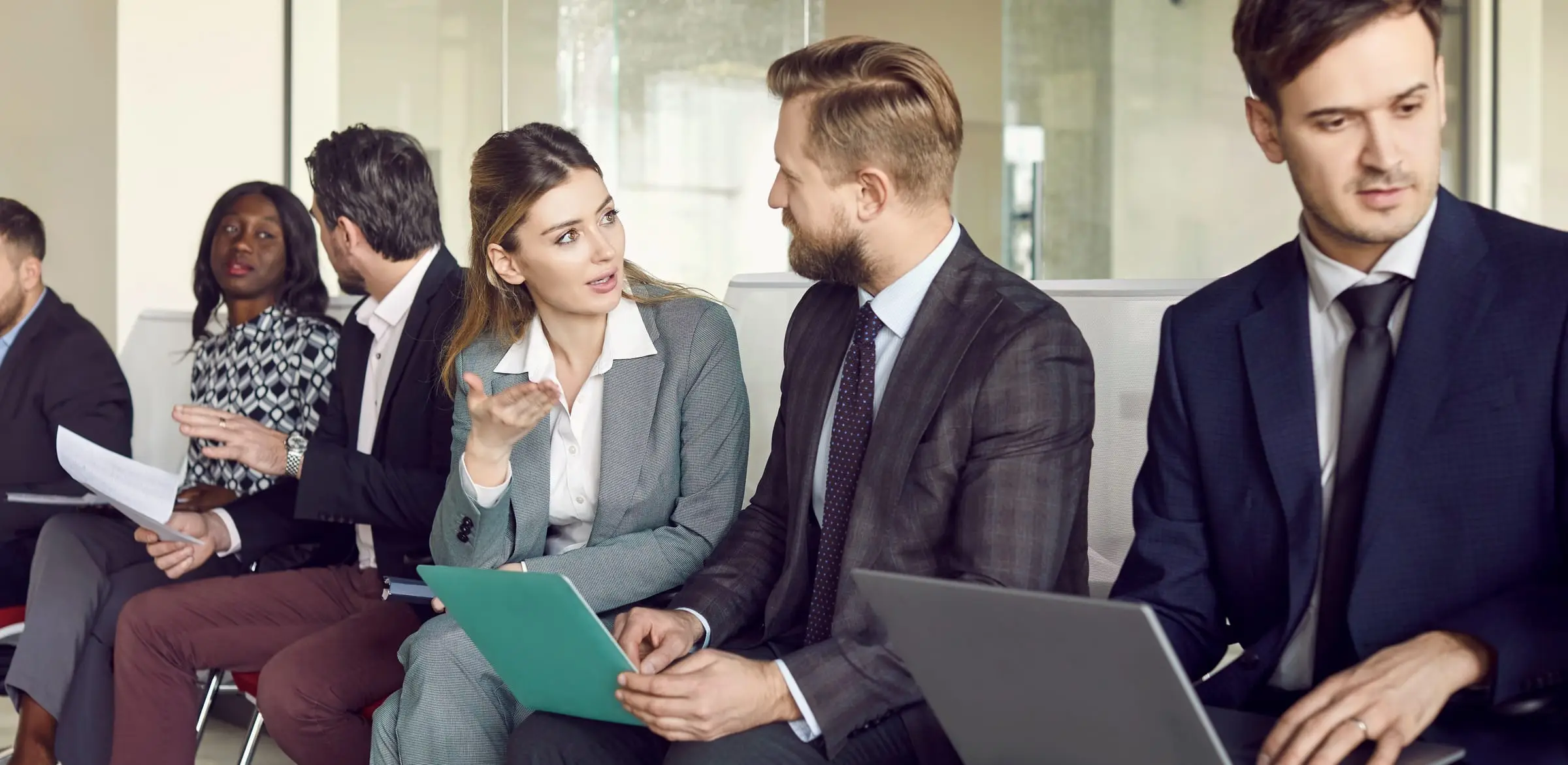 Candidates in business attire in conversation while waiting for interviews in a bright office